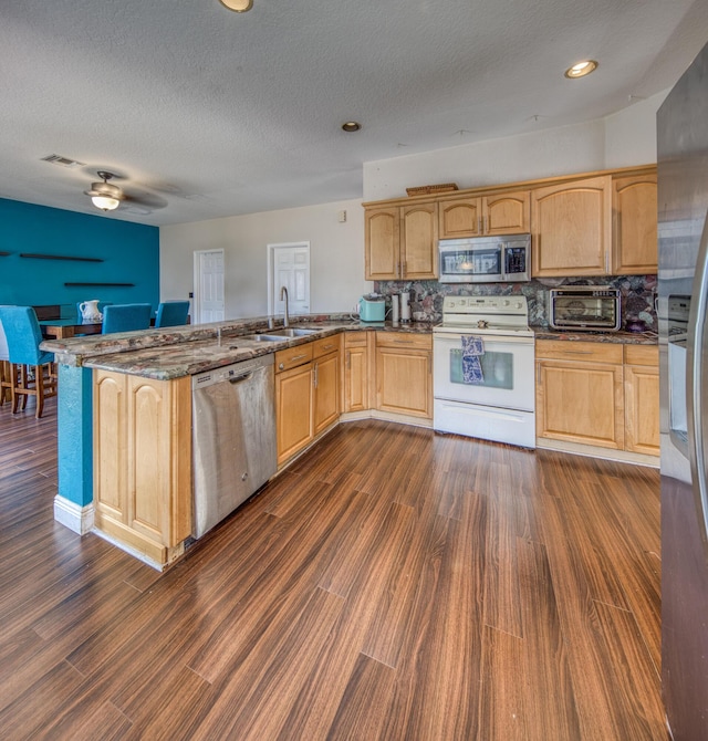 kitchen with a peninsula, appliances with stainless steel finishes, dark wood-type flooring, and dark stone countertops