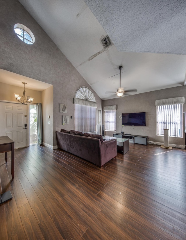 unfurnished living room with high vaulted ceiling, dark hardwood / wood-style flooring, ceiling fan with notable chandelier, and a wealth of natural light