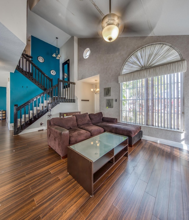 living room featuring baseboards, dark wood-style flooring, an inviting chandelier, stairs, and high vaulted ceiling