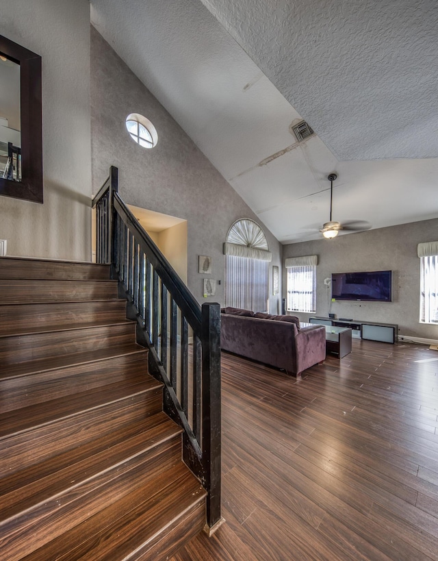 staircase with visible vents, ceiling fan, wood finished floors, a textured ceiling, and high vaulted ceiling