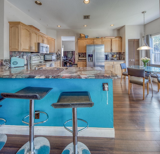 kitchen with stainless steel appliances, a peninsula, visible vents, dark countertops, and decorative light fixtures