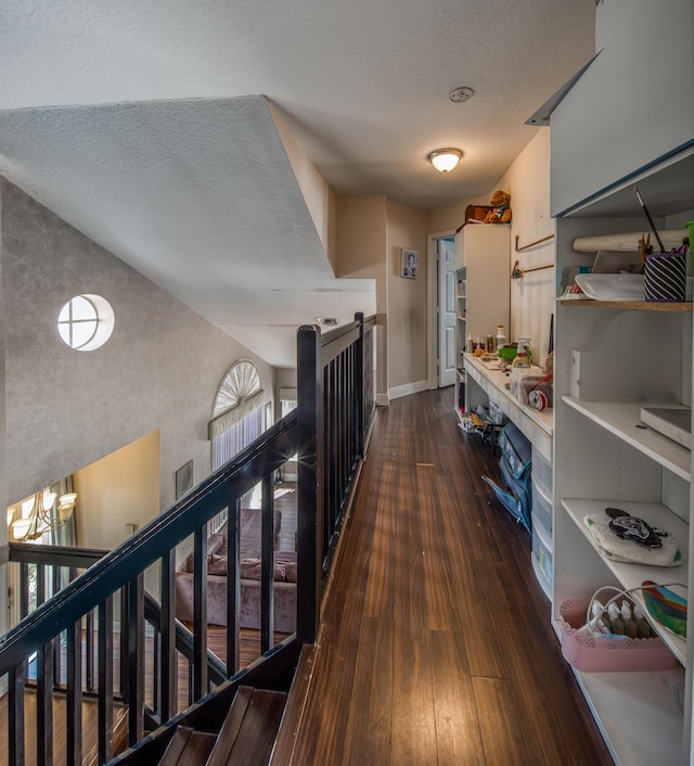 hall featuring a textured ceiling, dark wood finished floors, an upstairs landing, and baseboards