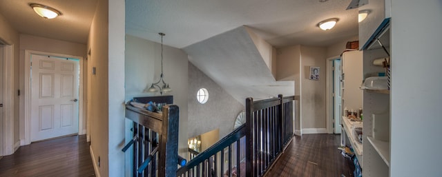 hallway with a textured ceiling, dark wood-type flooring, an upstairs landing, and baseboards