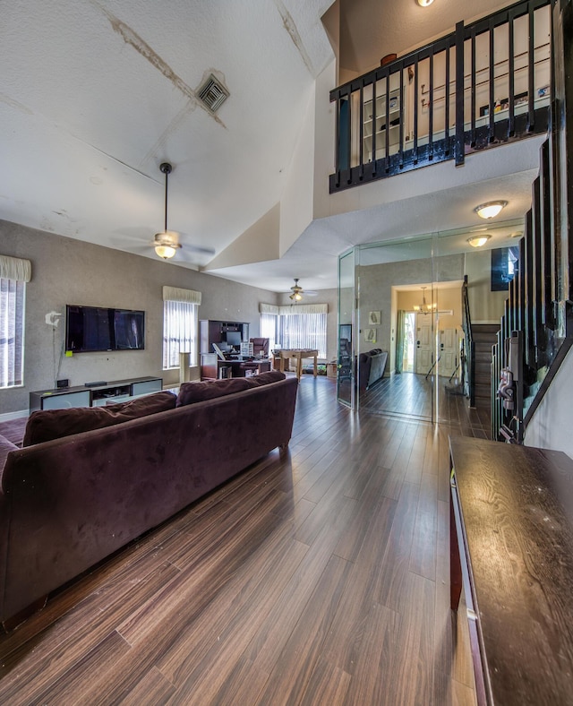 living area featuring visible vents, dark wood-type flooring, stairs, high vaulted ceiling, and ceiling fan with notable chandelier