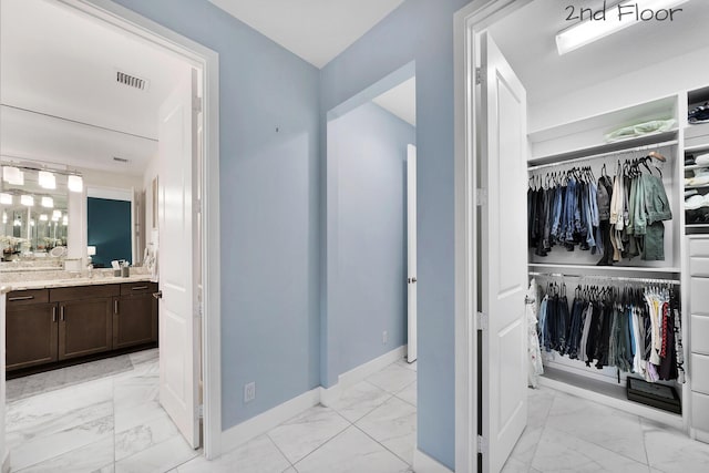 bathroom with marble finish floor, a spacious closet, baseboards, and vanity