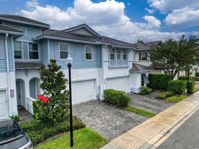 multi unit property featuring a garage, decorative driveway, a tile roof, and stucco siding