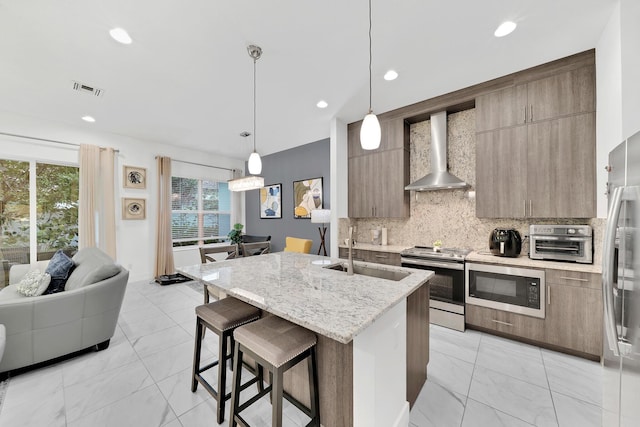 kitchen featuring a breakfast bar, a sink, stainless steel appliances, wall chimney range hood, and backsplash