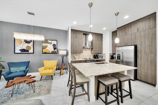 kitchen with stainless steel fridge with ice dispenser, a breakfast bar area, a sink, wall chimney range hood, and backsplash