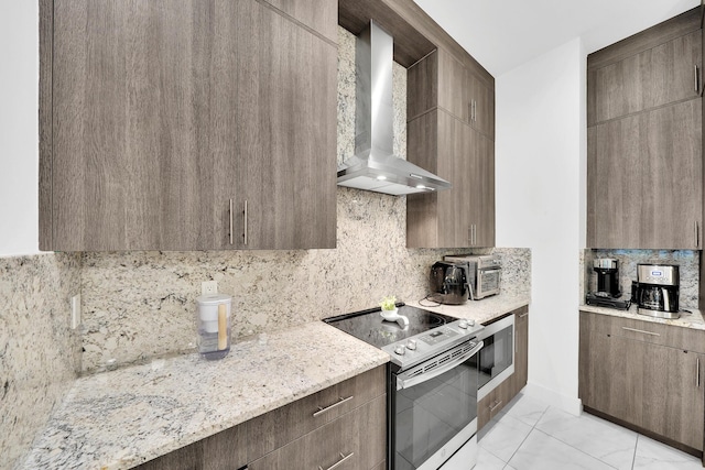 kitchen with light stone countertops, wall chimney range hood, stainless steel electric range oven, and backsplash