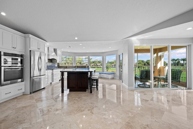 kitchen with a center island, custom exhaust hood, a kitchen breakfast bar, stainless steel appliances, and white cabinets