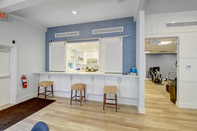 kitchen with white cabinetry, light hardwood / wood-style flooring, a breakfast bar area, and a barn door