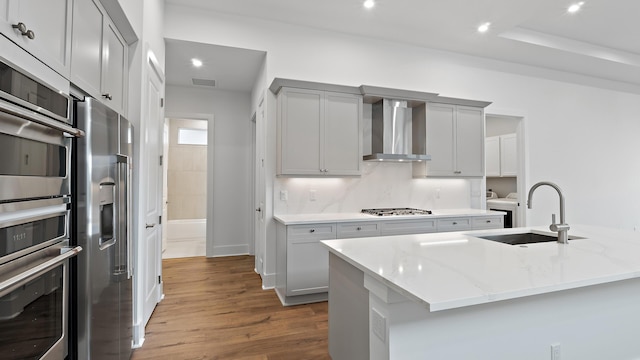 205 SE Via Sangro, Port Saint Lucie, FL 34952 - kitchen with wall chimney range hood, a sink, appliances with stainless steel finishes, dark wood finished floors, and light stone counters