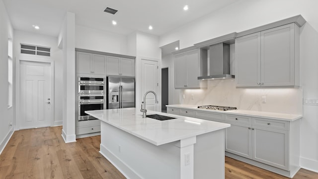 205 SE Via Sangro, Port Saint Lucie, FL 34952 - kitchen featuring appliances with stainless steel finishes, a sink, wall chimney range hood, gray cabinetry, and decorative backsplash