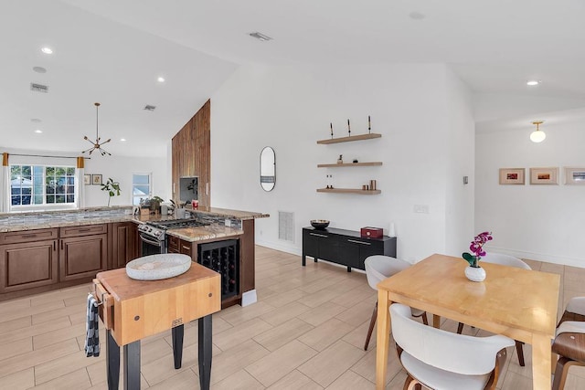 kitchen with lofted ceiling, light stone counters, wine cooler, stainless steel range with gas cooktop, and kitchen peninsula