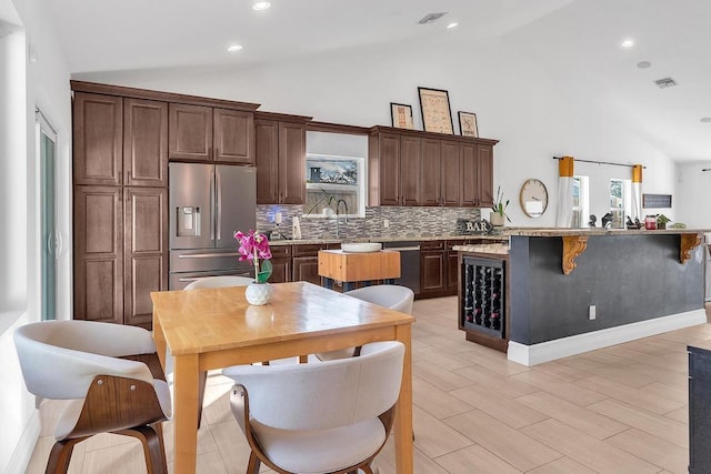 kitchen featuring a breakfast bar area, appliances with stainless steel finishes, high vaulted ceiling, decorative backsplash, and light wood-type flooring