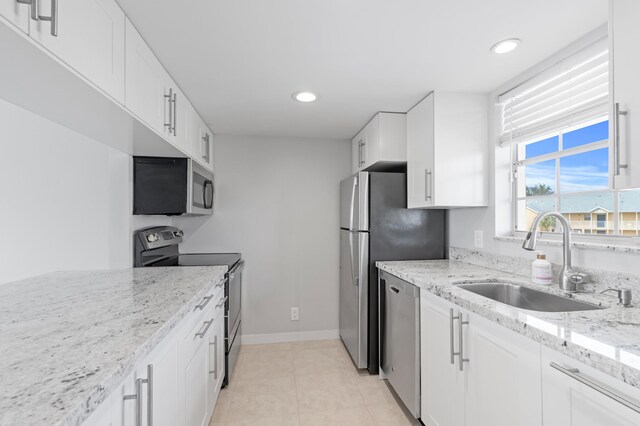 kitchen featuring appliances with stainless steel finishes, a sink, light stone counters, and white cabinets