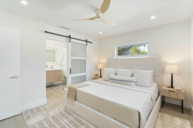 bedroom featuring radiator, ensuite bath, light wood-type flooring, ceiling fan, and a barn door