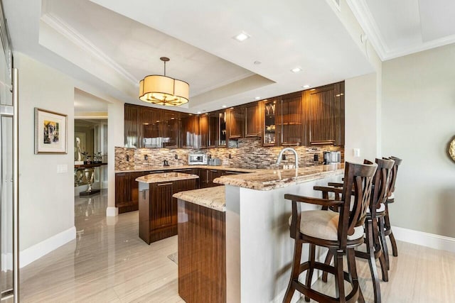 kitchen featuring kitchen peninsula, a tray ceiling, hanging light fixtures, light stone countertops, and a center island