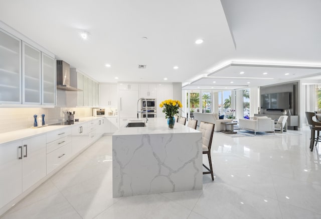 kitchen featuring white cabinets, a kitchen bar, wall chimney exhaust hood, and a large island