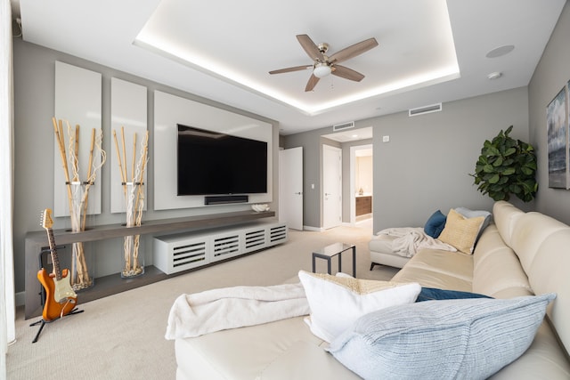 carpeted living room with a raised ceiling and ceiling fan