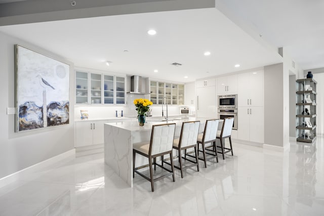 kitchen featuring white cabinetry, a breakfast bar area, stainless steel appliances, a spacious island, and wall chimney exhaust hood