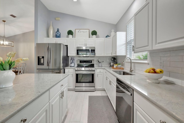 kitchen with pendant lighting, sink, appliances with stainless steel finishes, light stone counters, and white cabinets