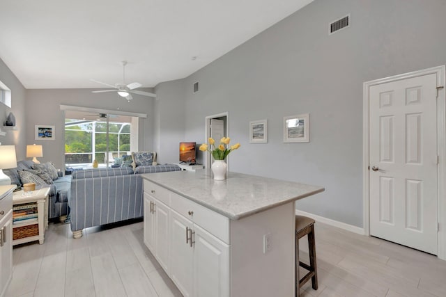 kitchen featuring a kitchen bar, white cabinetry, vaulted ceiling, a kitchen island, and ceiling fan