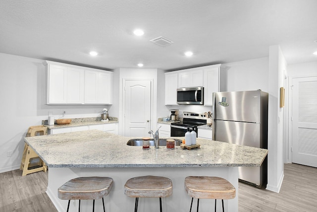 kitchen with an island with sink, sink, stainless steel appliances, and white cabinetry