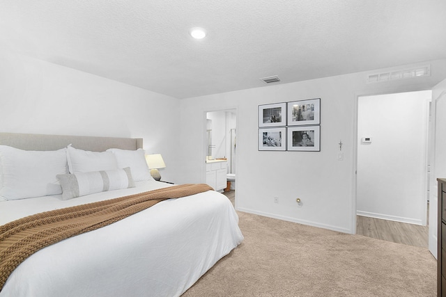 bedroom featuring light carpet, a textured ceiling, and ensuite bath