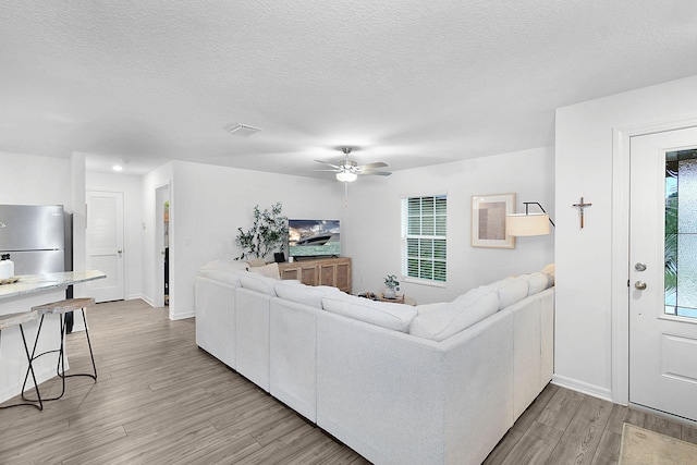 living room with a textured ceiling, ceiling fan, a healthy amount of sunlight, and light hardwood / wood-style floors