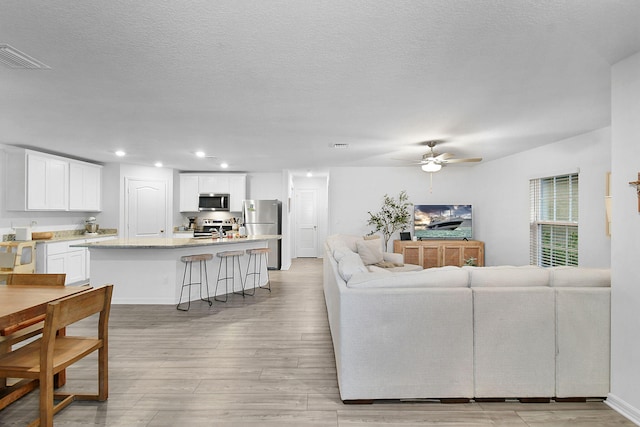 living room featuring a textured ceiling, ceiling fan, and light hardwood / wood-style flooring