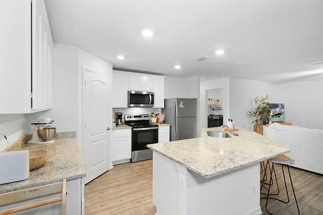 kitchen with a breakfast bar area, appliances with stainless steel finishes, white cabinetry, and an island with sink