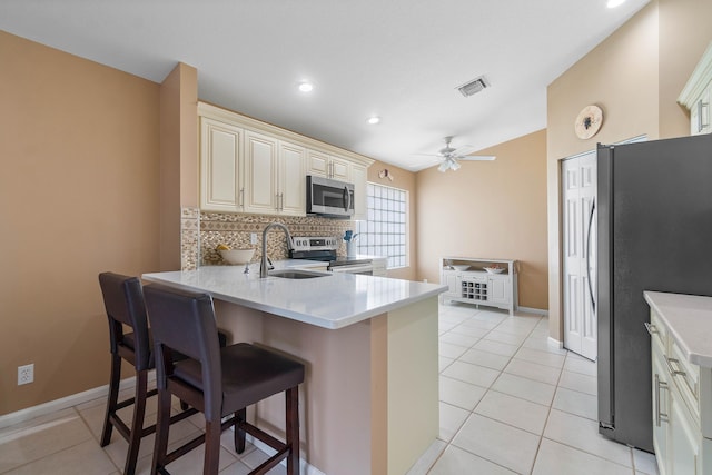 kitchen with kitchen peninsula, cream cabinetry, stainless steel appliances, and a kitchen bar