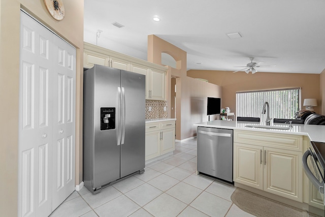 kitchen with lofted ceiling, decorative backsplash, sink, appliances with stainless steel finishes, and cream cabinets