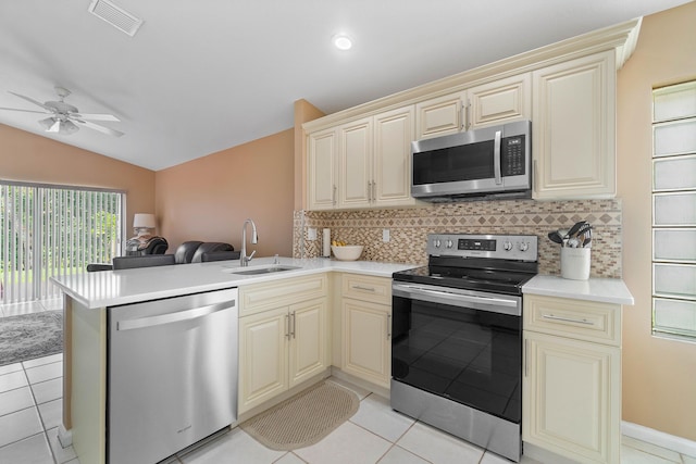 kitchen featuring vaulted ceiling, kitchen peninsula, sink, appliances with stainless steel finishes, and cream cabinetry