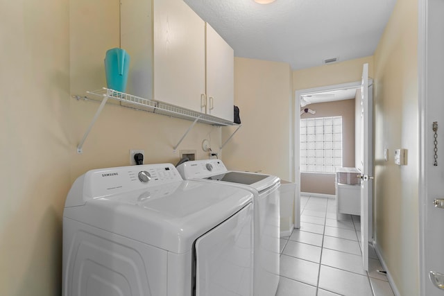 laundry room featuring a textured ceiling, cabinets, light tile patterned flooring, and independent washer and dryer