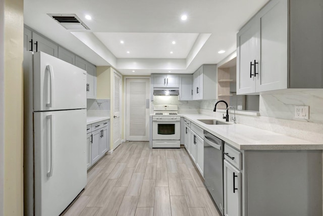 kitchen with white appliances, sink, backsplash, a raised ceiling, and light stone counters