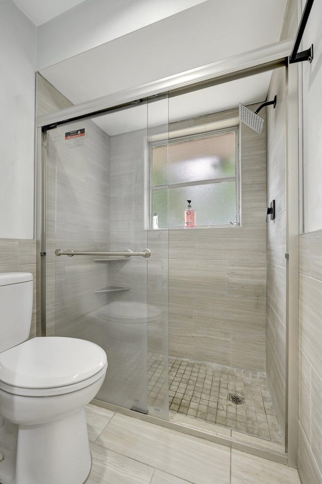 bathroom with toilet, a shower with door, and tile patterned flooring