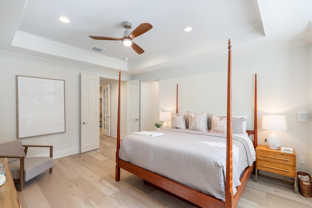 bedroom with ceiling fan, a tray ceiling, crown molding, and light wood-type flooring