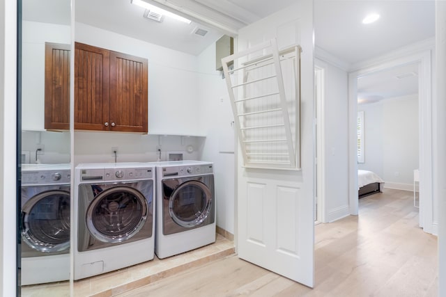 clothes washing area with cabinets, light hardwood / wood-style flooring, and washing machine and clothes dryer