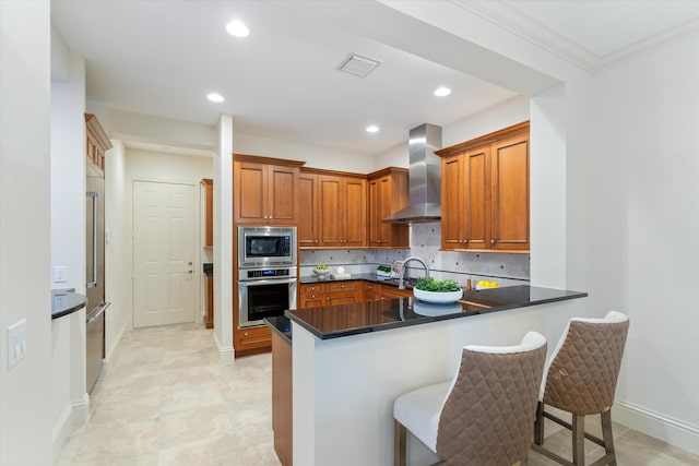 kitchen with backsplash, kitchen peninsula, a kitchen breakfast bar, stainless steel appliances, and wall chimney exhaust hood