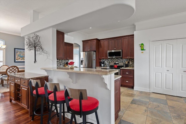 kitchen with a kitchen island, a kitchen bar, decorative backsplash, crown molding, and appliances with stainless steel finishes