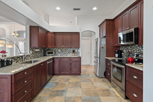 kitchen with appliances with stainless steel finishes, tasteful backsplash, ornamental molding, light stone counters, and sink