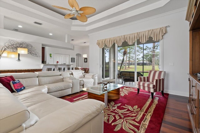 living room featuring ceiling fan, dark hardwood / wood-style flooring, crown molding, and a tray ceiling