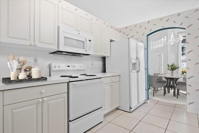 kitchen featuring white appliances, white cabinetry, decorative backsplash, a chandelier, and light tile patterned flooring