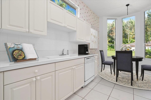 kitchen with light tile patterned floors, white dishwasher, hanging light fixtures, white cabinets, and sink