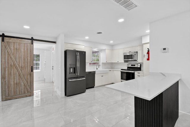 2112 N 14th Ter, Hollywood, FL 33020 - kitchen with appliances with stainless steel finishes, a barn door, light countertops, a peninsula, and decorative backsplash