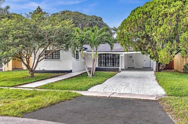 view of front of property with a front lawn, decorative driveway, an attached carport, and stucco siding