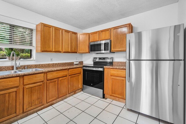 kitchen with light tile patterned floors, sink, a textured ceiling, and appliances with stainless steel finishes