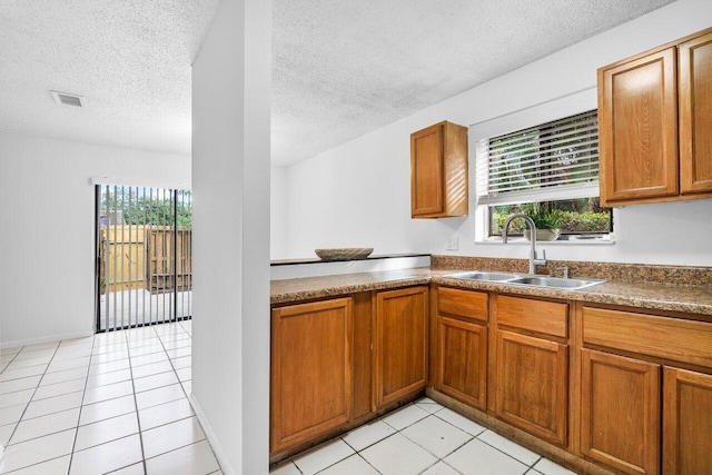 kitchen with sink, a textured ceiling, light tile patterned floors, and a healthy amount of sunlight